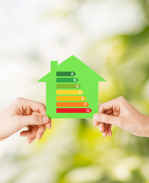 energy saving, real estate and family home concept - closeup of couple hands holding green paper house with energy efficiency rating
